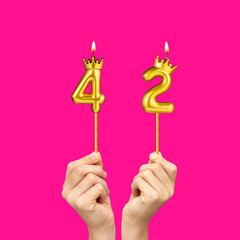 Birthday on a fuchsia background with the number 42 - Hands holding number-shaped candles