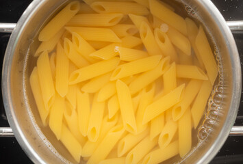 Uncooked penne pasta in boiling water in a pot.