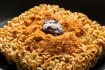 Close-up of raw instant noodles with spicy seasoning powder on top in a black bowl.