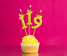 Birthday celebration with number 119 candle - Yellow cupcake on a pink background