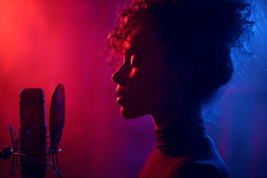 Singer performs in dramatic lighting with microphone in a creative studio setting during a nighttime session