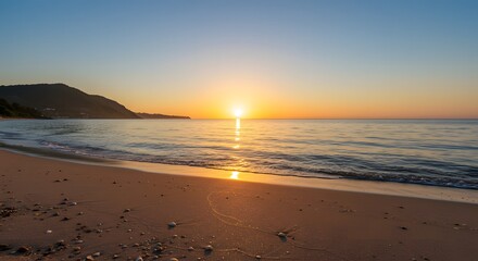 A beach scene featuring the sun setting over the ocean with a mountain in the distant background view