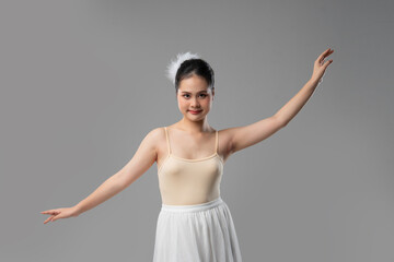 Young ballet dancer in a light-colored leotard and white tutu performs gracefully on a gray backdrop