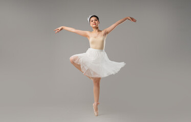 A young ballerina poses en pointe in a studio wearing a tutu leotard and headpiece