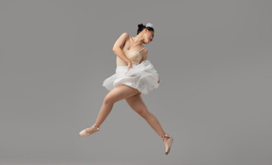 A dancer in a white tutu and pointe shoes leaps with grace against a light grey background