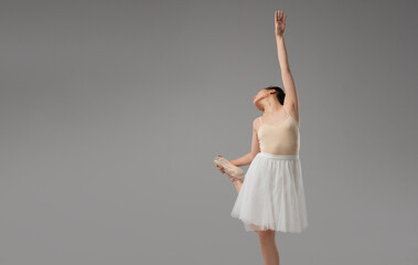 Ballerina gracefully poses with pointe shoes in hand extending arm upwards against gray background