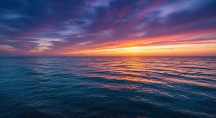 Ocean water reflects a vibrant sunset with colorful clouds in the sky.