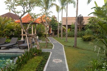 A serene pathway leads through lush tropical gardens in Ubud, Bali, Indonesia. The path connects...
