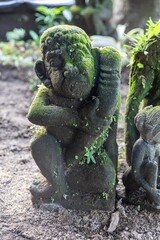 Moss-covered stone statues of Balinese figures sit in a garden in Ubud, Bali, Indonesia. The...