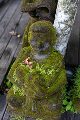 A moss-covered stone statue of a Balinese figure sits serenely in Ubud, Bali, Indonesia. The...
