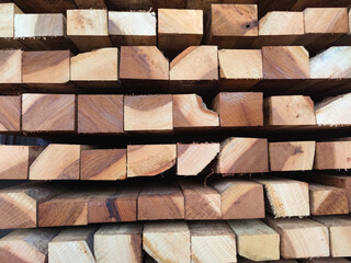 A close-up image of stacked wooden planks with visible natural grain and texture. The timber beams are arranged in a pattern, showcasing the raw and unfinished state of the wood
