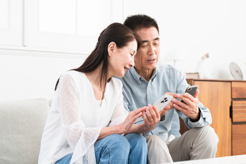 ソファーに座ってスマートフォンを操作している熟年夫婦　ライフスタイルイメージ