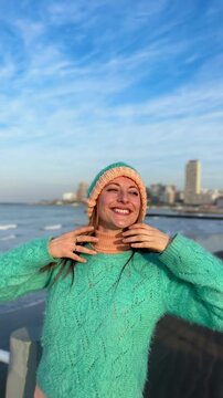 Playful ginger-haired woman, 30s, outdoors by sea, in a colorful outfit and fun hat. Laughing and being silly.  Bright, cheerful spring or fall vibe.