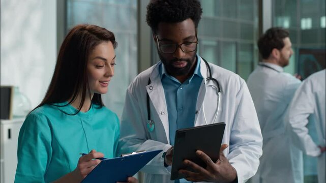 Doctors two medical people Caucasian woman female student doctor and African American man male therapist intern holding tablets discuss health test results treatment diagnosis talking clinic hospital