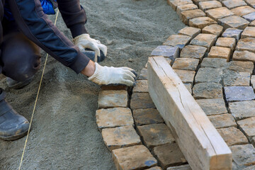 Construction worker carefully placing cobblestones on sandy foundation under works day