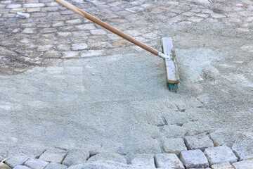 Worker levels sand on newly laid cobblestone path in bright clear outdoor setting.