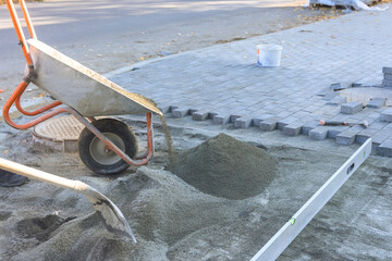 Workers are preparing to install pavers on street using wheelbarrow for sand leveling tools for...