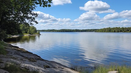 Serene lakeside view on a sunny day, featuring calm water reflecting the sky, lush greenery, and rocky shoreline