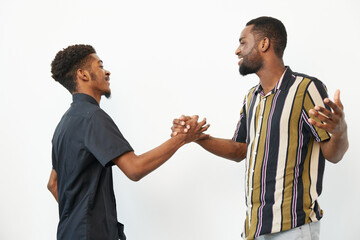 Two joyful African American men greeting each other with smiles and handshakes against a bright...