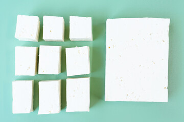 Whole tofu and sliced on green background, top view.