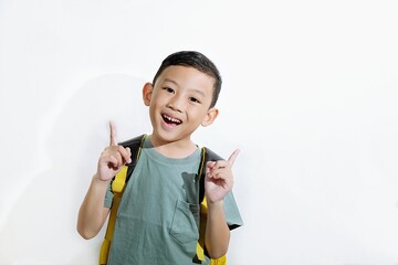 Happy school boy with backpack smiling and pointing with both index fingers on white background. Great for education, childhood, or motivation themes.