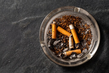 Ashtray with cigarette butts and tobacco remnants on dark surface