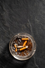 Ashtray with Used Cigarette Butts and Ash on Dark Background