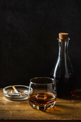 Elegant Whiskey Glass with Bottle and Ashtray on Wooden Surface