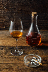 Glass of Amber Liquor with Bottle and Ashtray on Rustic Wooden Table