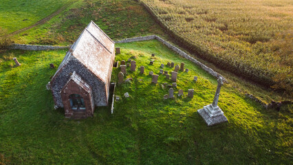 Aerial view of Kirkmadrine Chapel, a historic church with a graveyard, surrounded by vibrant green fields under a soft, natural light