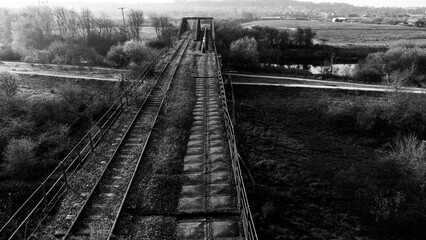 Aerial black and white of an old, derelict railway bridge with overgrown tracks