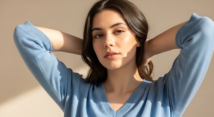 Portrait of a woman with hands behind her head wearing a blue sweater indoors