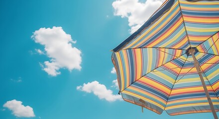 View looking up at a colorful striped beach umbrella against a blue sky day