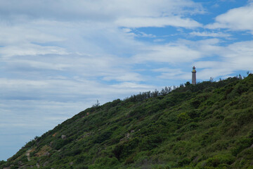 Solitary Dai Lanh lighthouse stands tall against a sky dotted with white clouds in Vietnam. Guidance, solitude, hope, and resilience, faithfully watching over the seas.