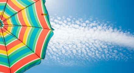 View of a striped beach umbrella against a blue sky with scattered clouds