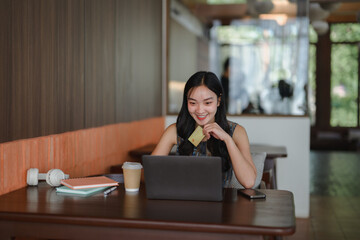 Young asian woman shopping online using laptop and credit card in cafe