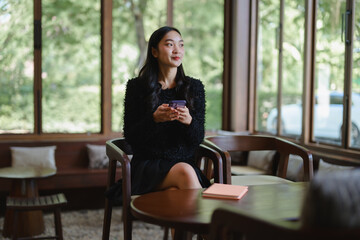Businesswoman holding smartphone thinking about future projects in modern cafe
