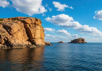 Rocky island formation in a tranquil blue sea under a bright sky with scattered clouds