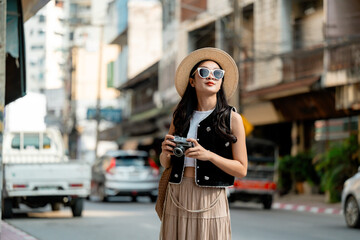 Young woman tourist exploring city street holding vintage camera