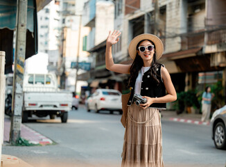 Fototapeta premium Young woman tourist hailing a taxi in Bangkok, Thailand, holding a vintage camera
