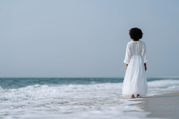 woman in white linen dress standing at the edge of the ocean, looking at horizon, soft focus, 