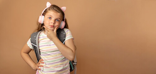 Banner with place for text. Portrait of a thoughtful little girl in headphones with a school...