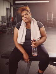 A woman sits in the gym after a workout with a bottle of water and a towel