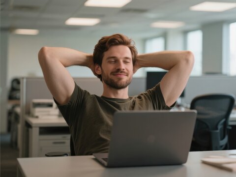 30-year-old caucasian man relaxing with hands behind head in front of laptop in modern office