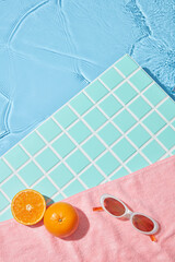 Two fresh oranges and retro sunglasses on pink towel by the pool. Soft water ripples meet clean mosaic tile in sharp summer light. Ideal setting for skincare mockups and tropical packaging visuals.