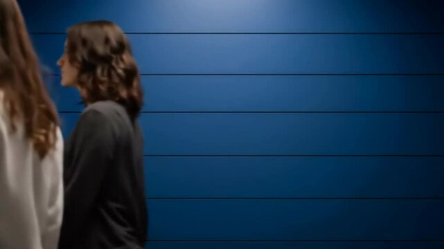 Two women walking past a dark blue wall in a modern setting, ideal for fashion and lifestyle promotions