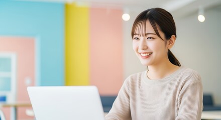 カラフルなオフィスでPC作業する笑顔の女性