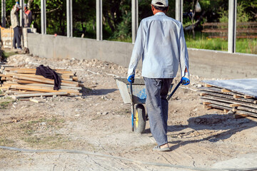 Construction worker pushing barrow with concrete at building site