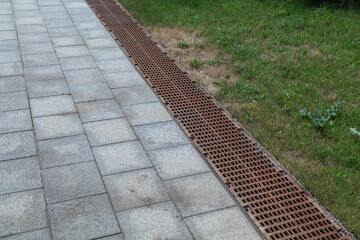 iron grate of a drainage system for storm water drainage from a pedestrian sidewalk near a green...