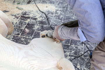 Man is carving a wooden sculpture with a power tool